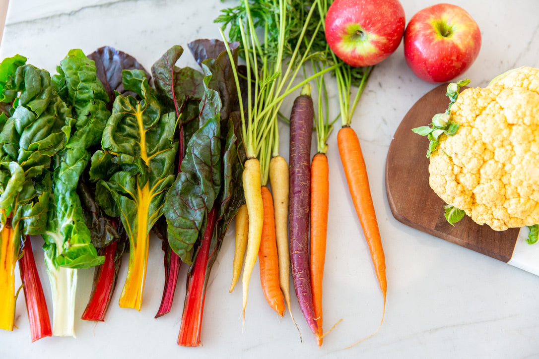 Nutrition by Gina; picture of colorful swiss chard, different colored garden fresh carrots, and cauliflower on marble countertop