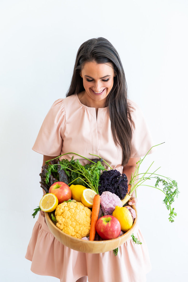 Nutrition by Gina; Registered Dietitian Lilley holding a basket full of colorful fruits and vegetables.